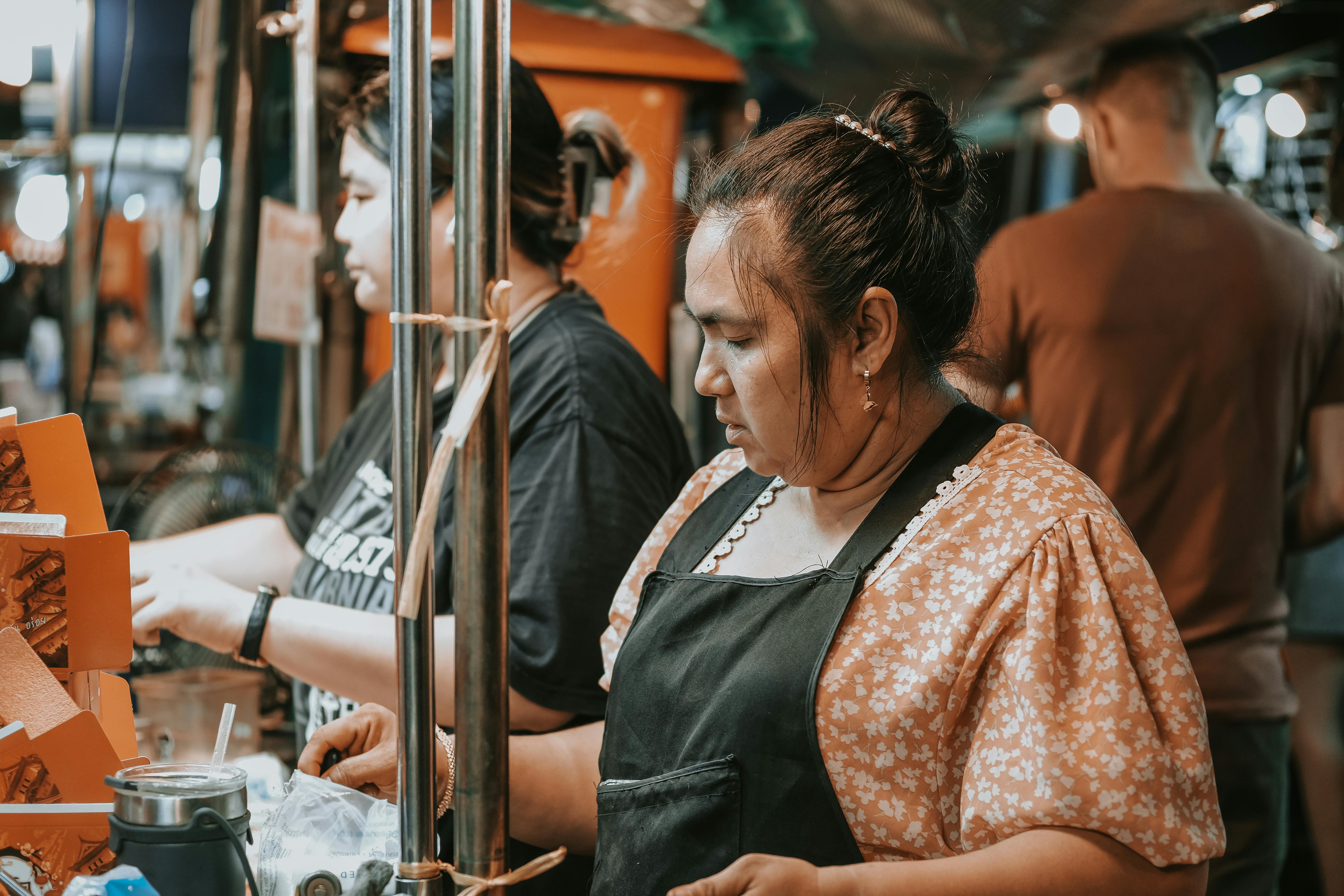 Two women in aprons are working at a food stand