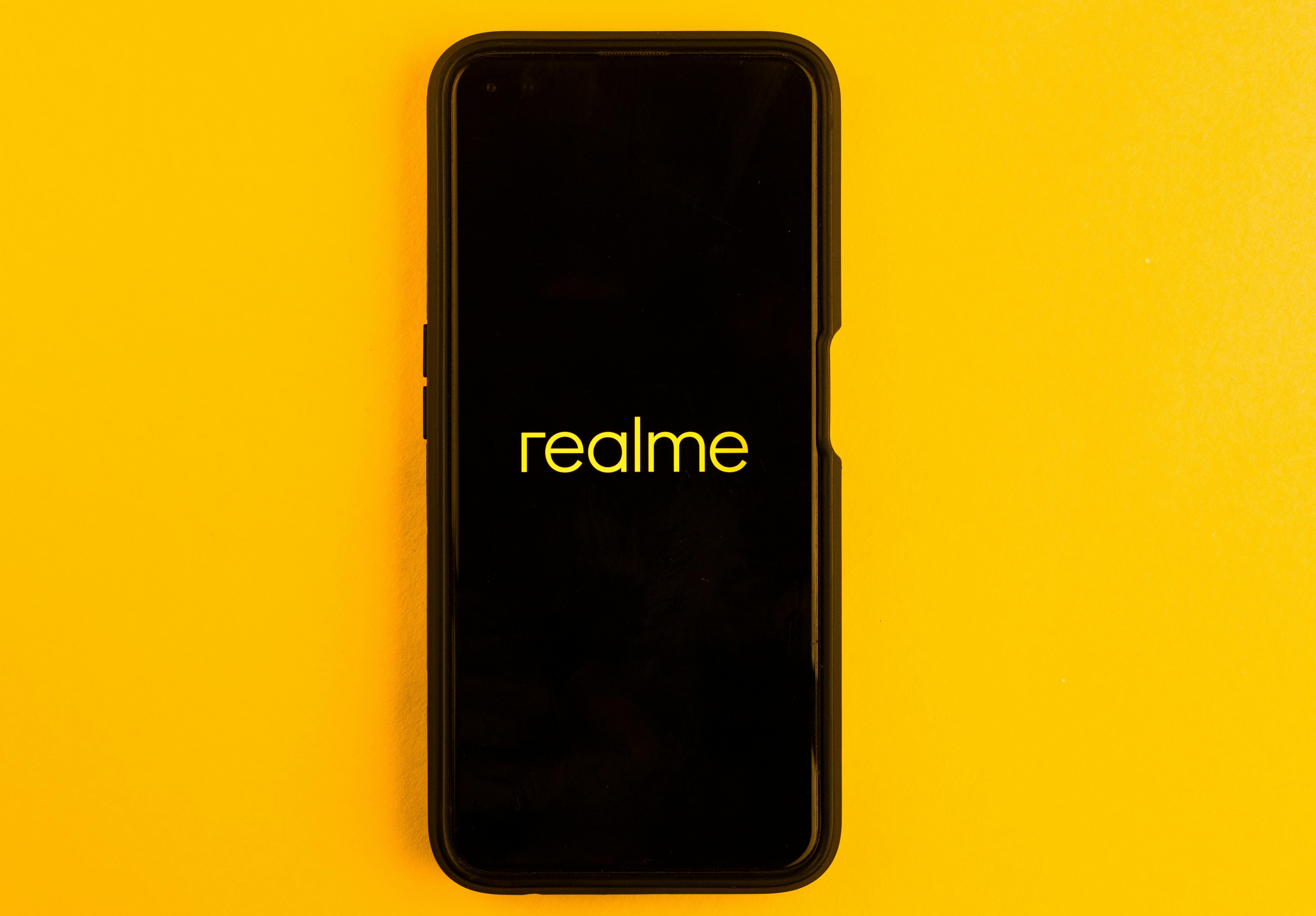 In this photo illustration the Realme logo seen displayed on a smartphone and on the background