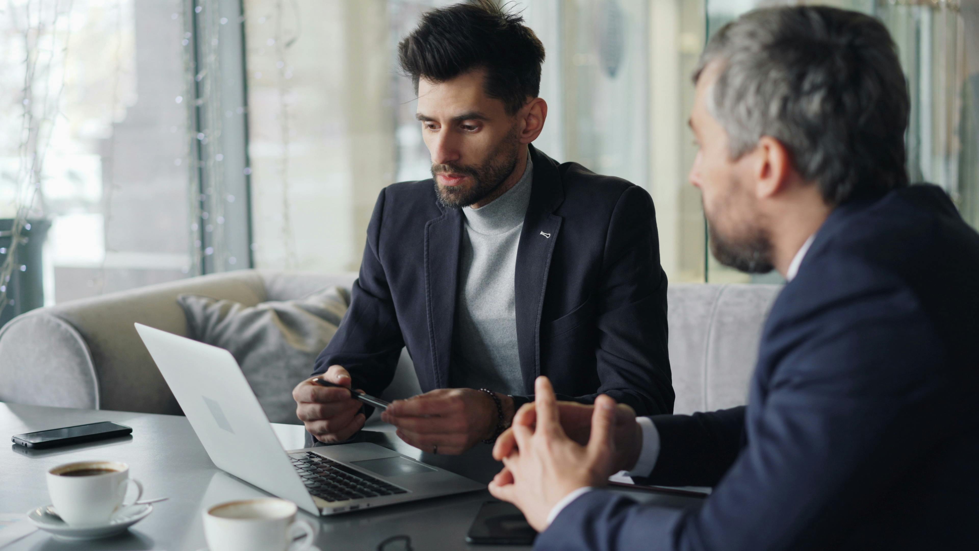 Two men in business attire sitting at a table with laptops