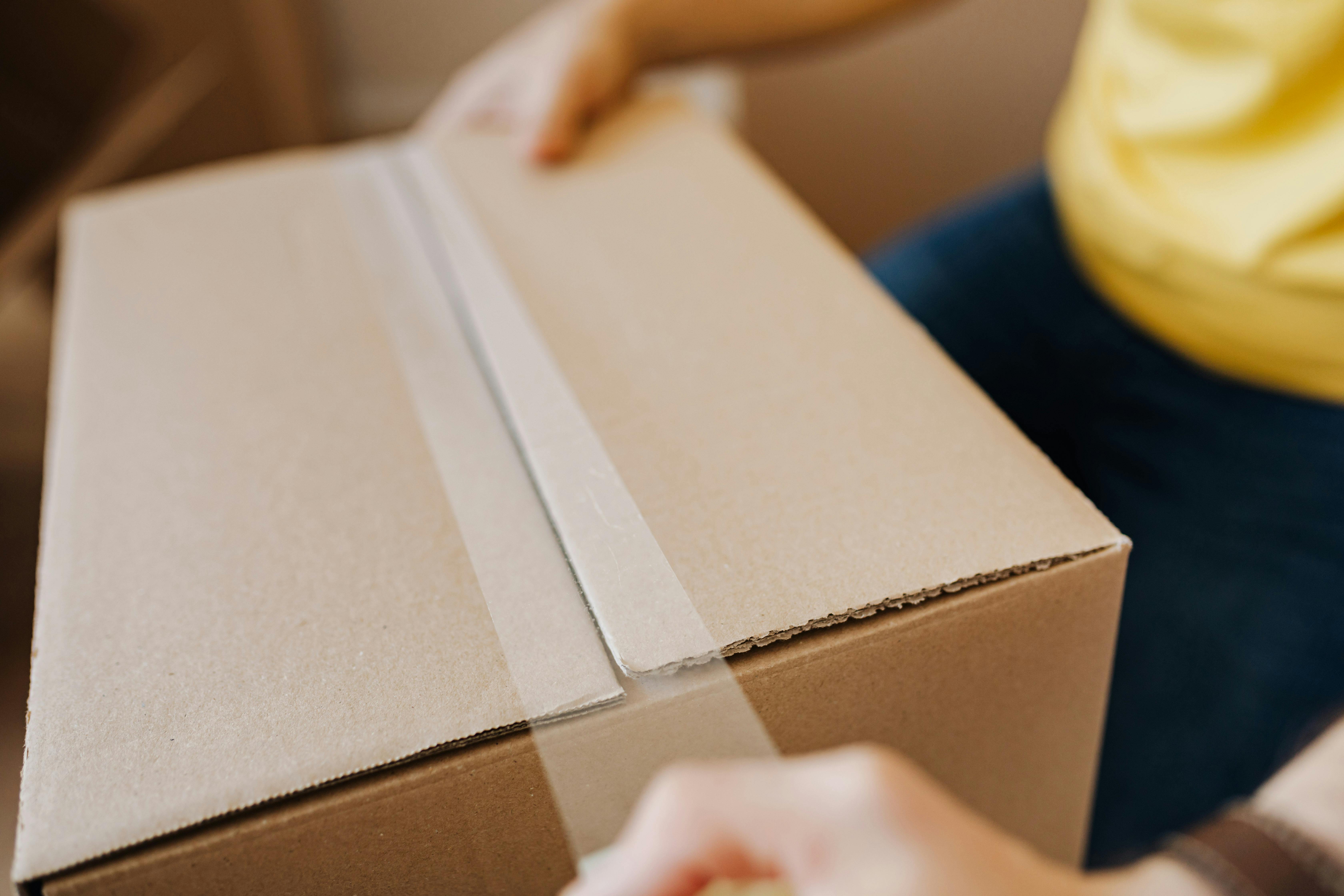 Crop man sealing cardboard box with tape