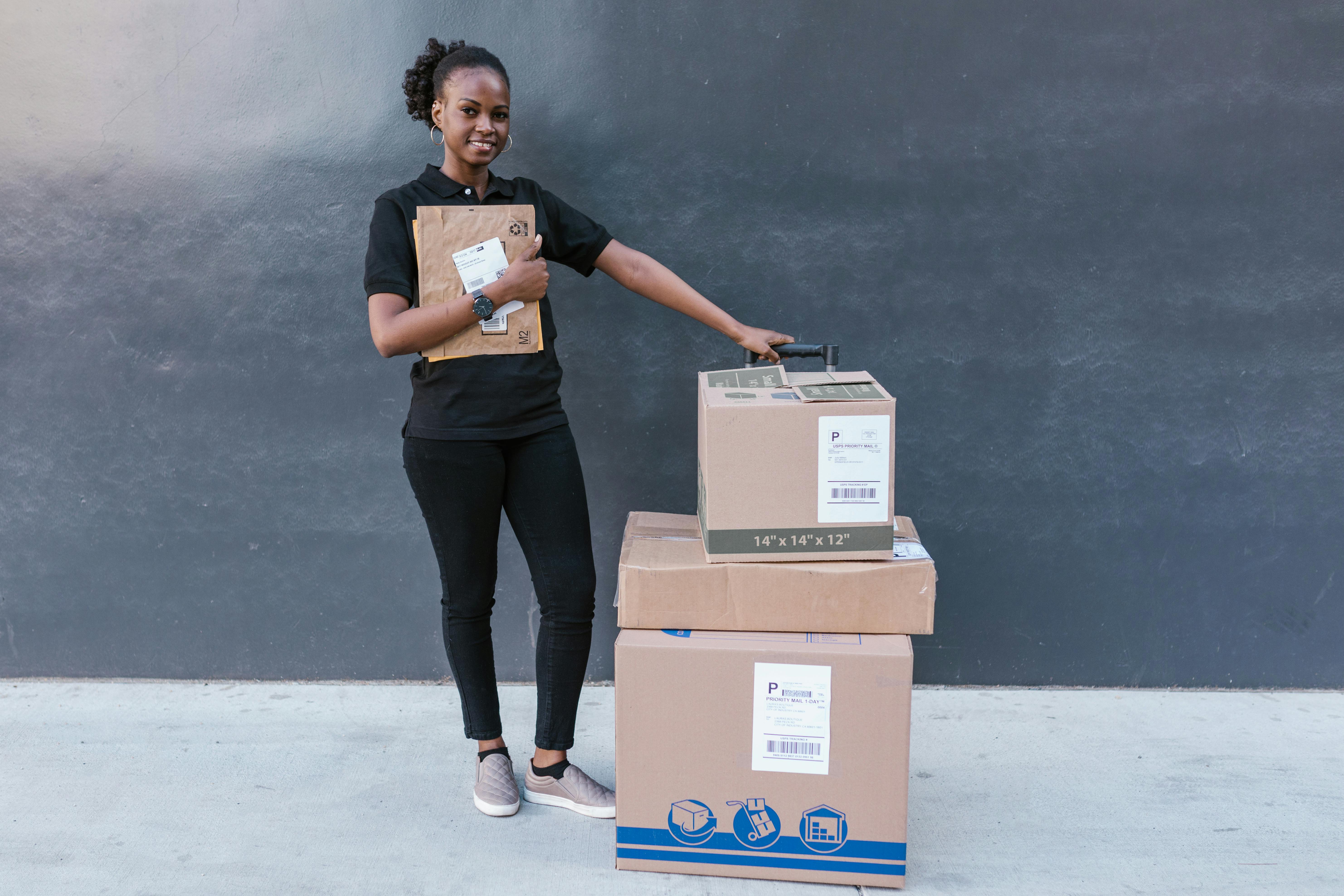 Woman in Black T-shirt and Black Pants Holding Brown Cardboard Box