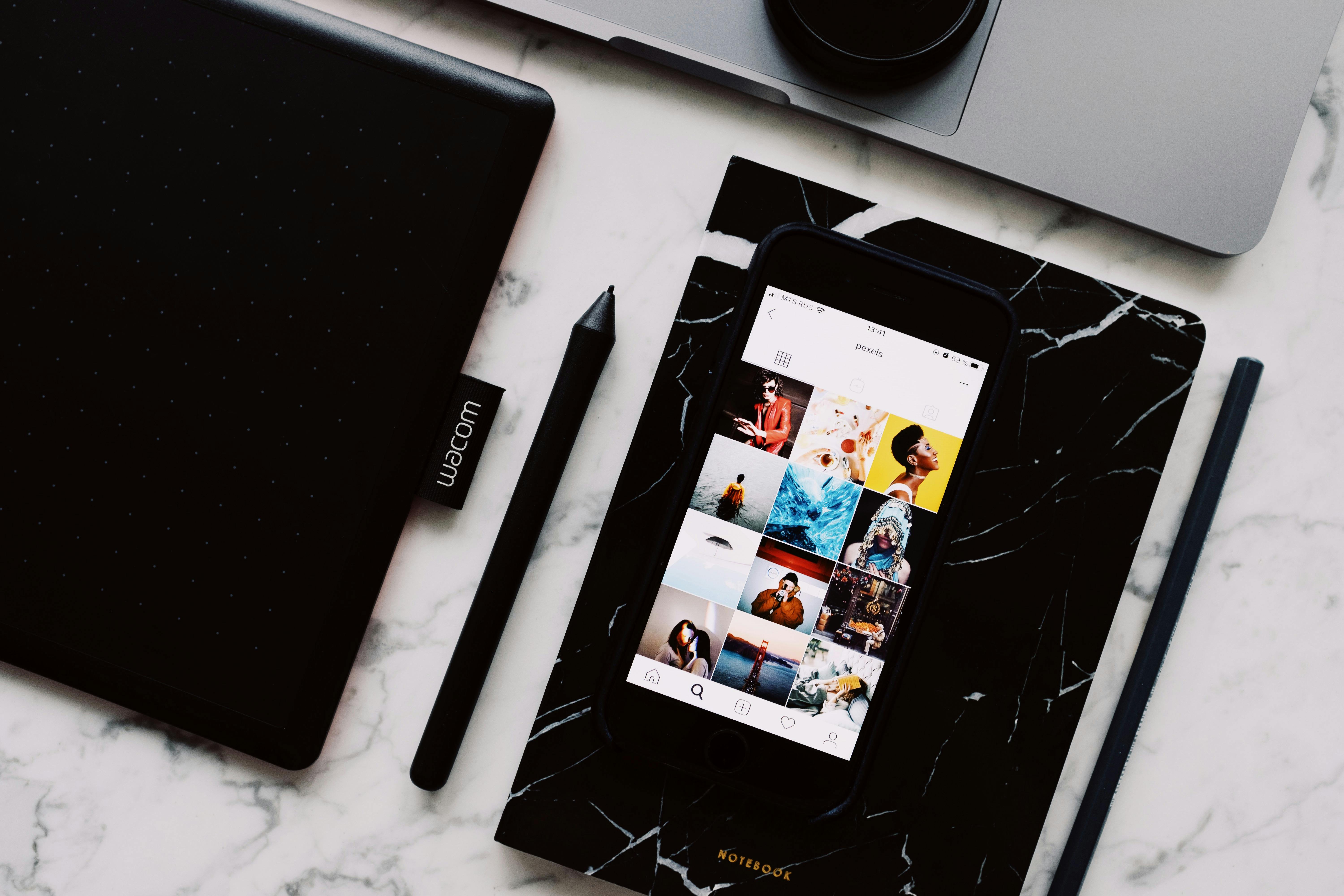 From above of marble table with black textbook and cellphone above with opened app showing interesting photo gallery on screen